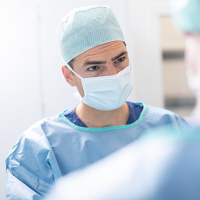 A person wearing surgical scrubs and mask.